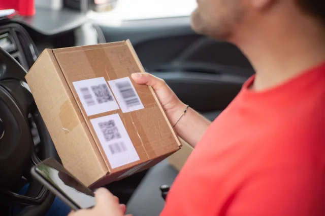Close-up of a person holding a package with QR codes inside a car, emphasizing delivery and technology. Which packaging marketing attribution methods actually work for UK brands?
